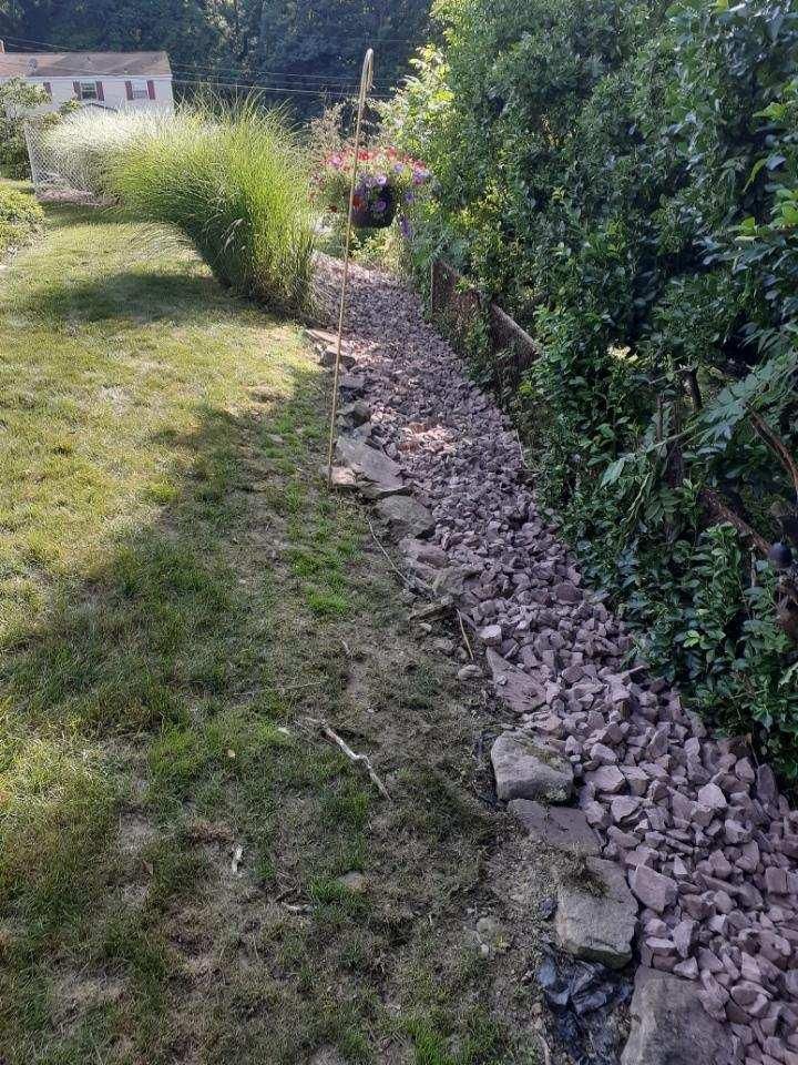A rocky garden bed alongside grass and green bushes.