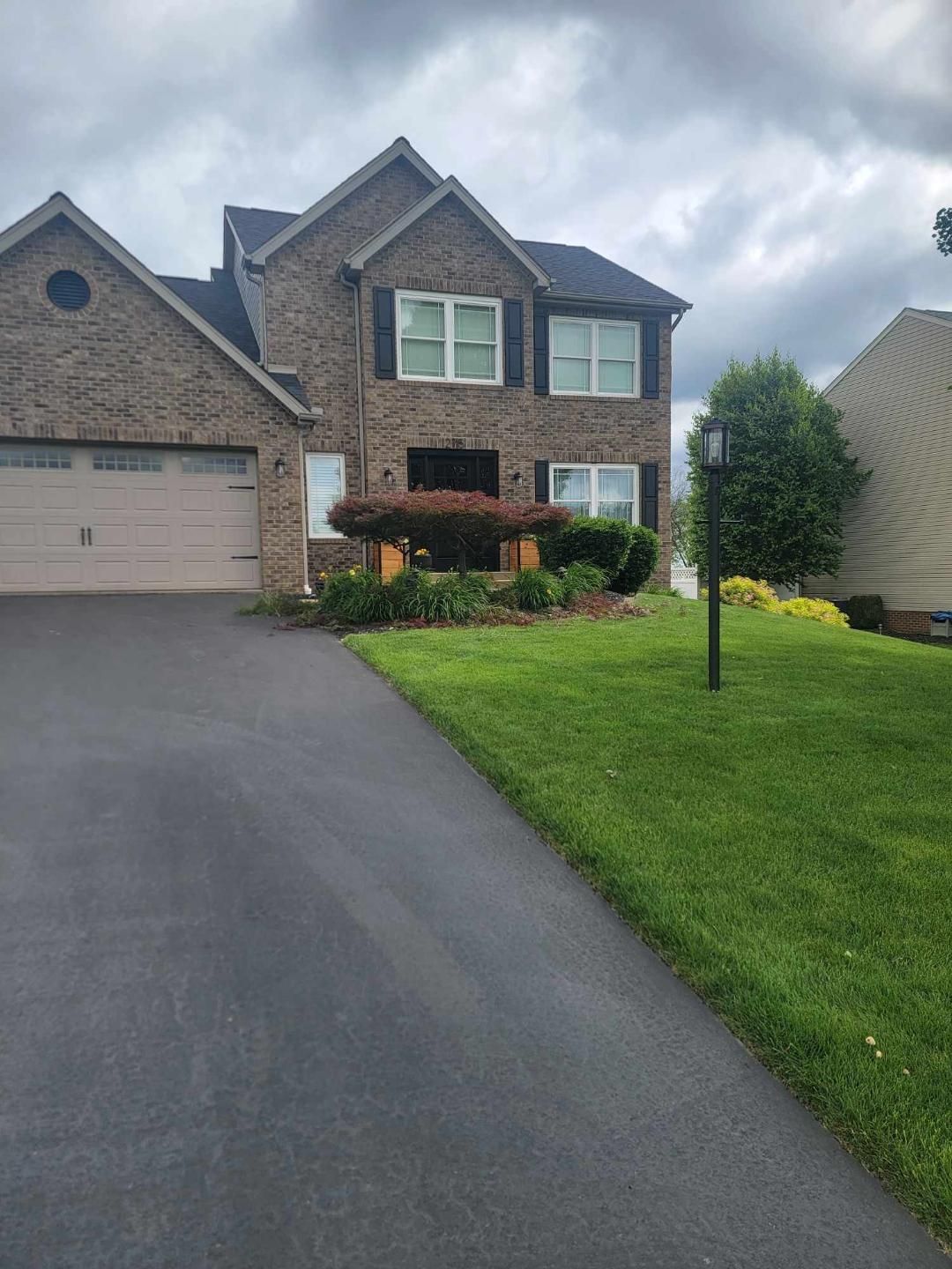 Two-story brick house with a dark driveway and well-manicured lawn under an overcast sky.