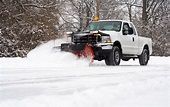 White snowplow truck clearing snow from a snow-covered field.