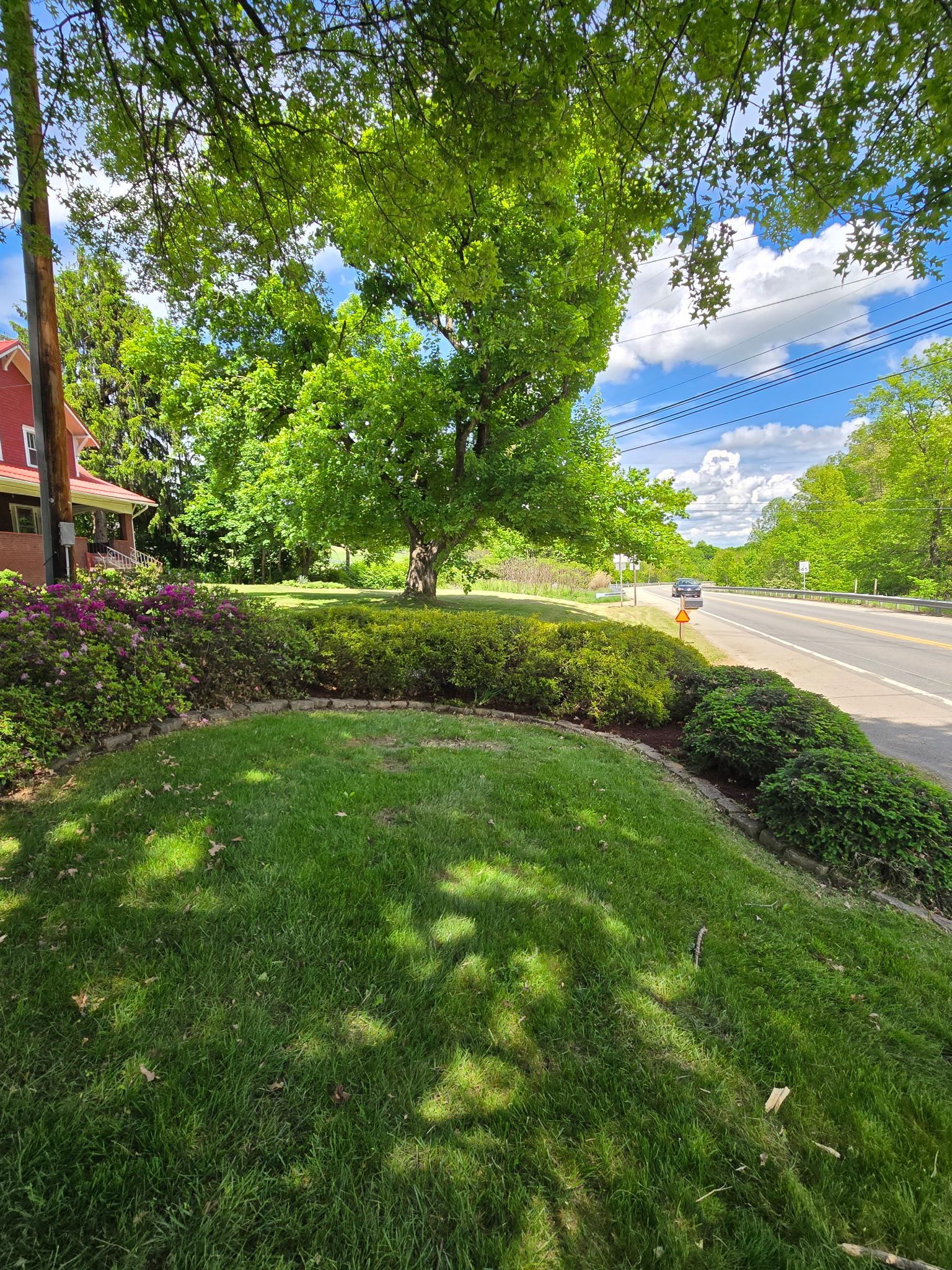 Lush green lawn and hedges border a tree-lined street under a partly cloudy sky.