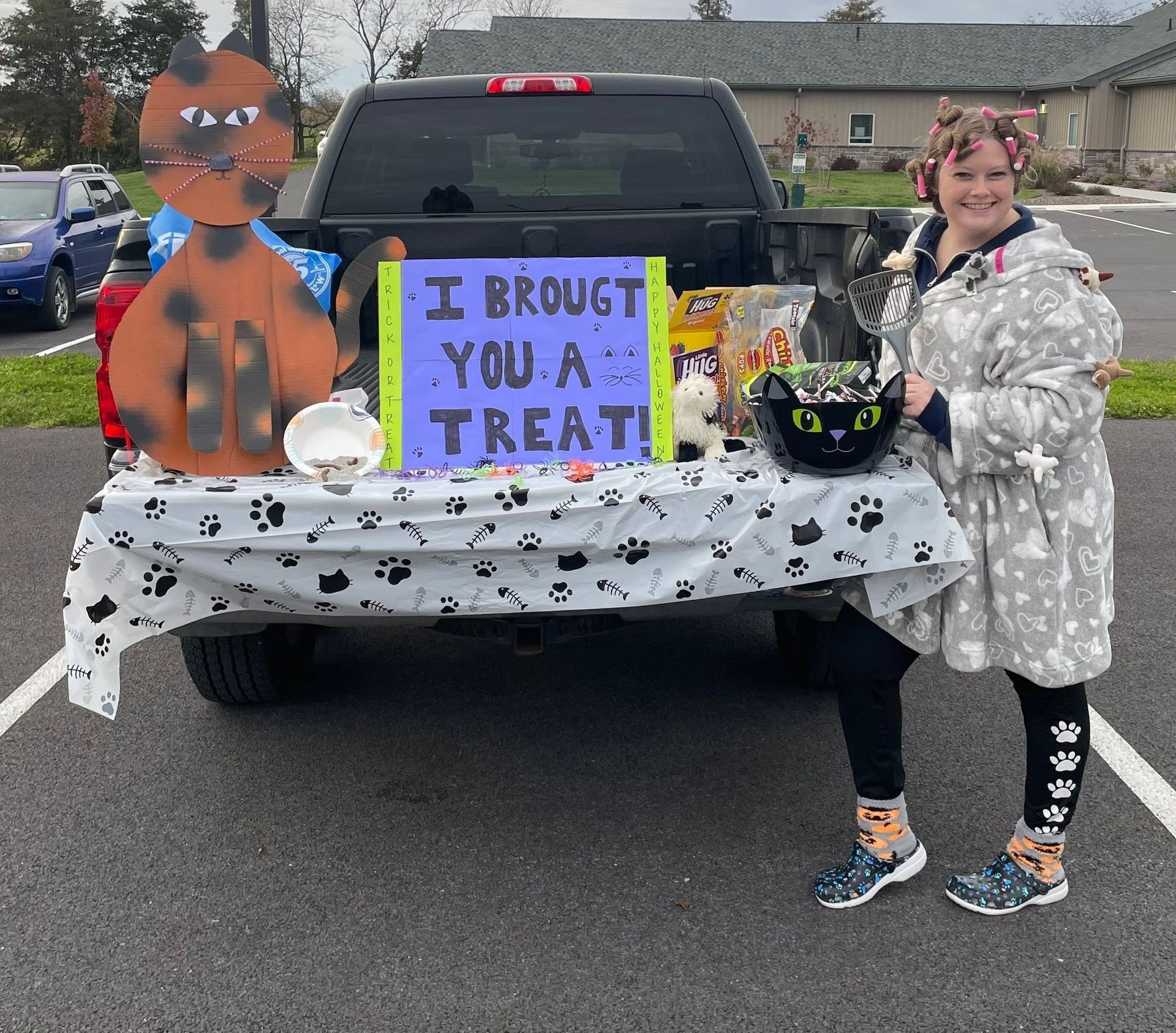 Costumed children at a trunk-or-treat table with a sign reading “I brought you a treat”