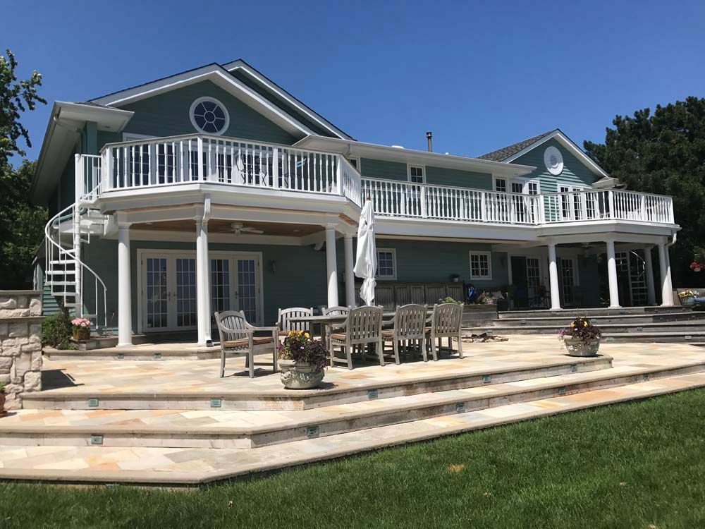 Large seaside house with white balconies and patio deck, viewed from a grassy yard under a clear blue sky
