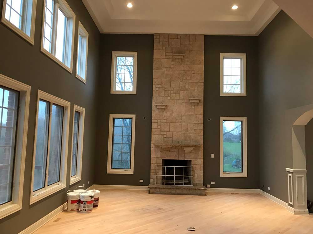 Empty living room with high ceiling, tall windows, stone fireplace, and unfinished hardwood floor