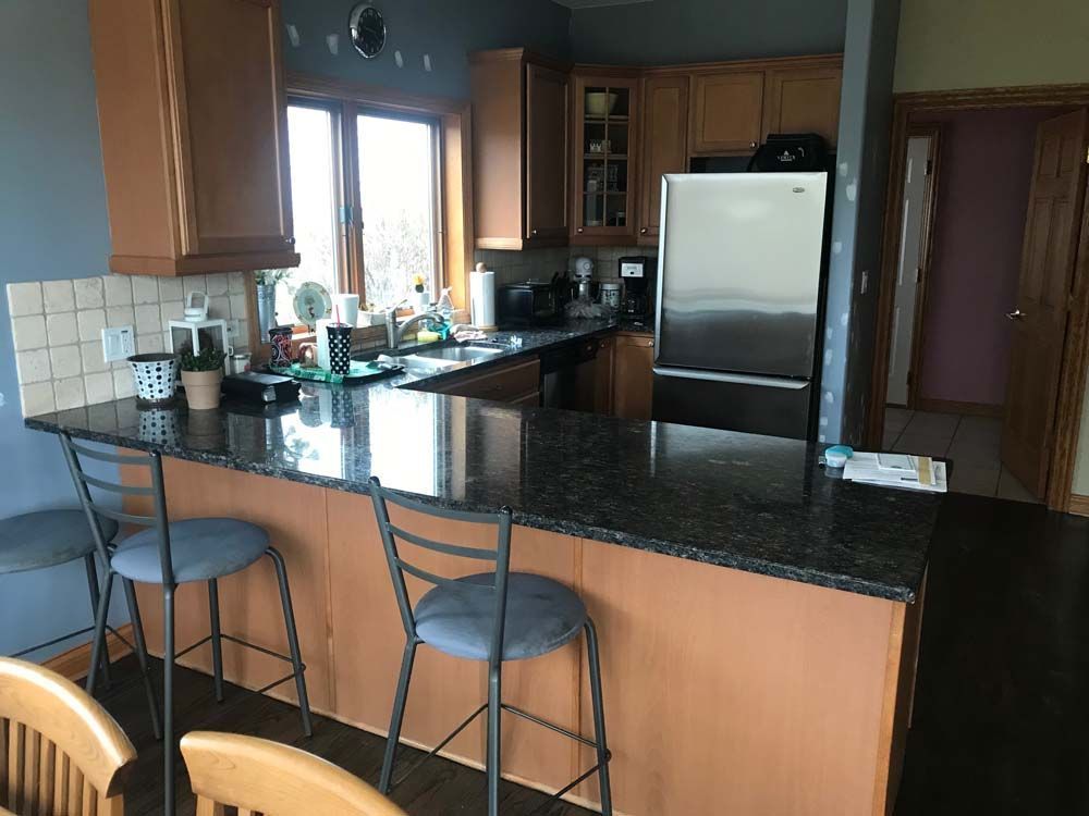 Kitchen with granite island, two stools, stainless refrigerator, and wood cabinets