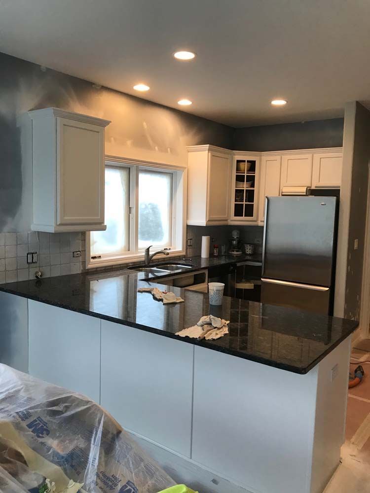 Modern kitchen with black granite island, white cabinets, stainless fridge, and recessed lighting