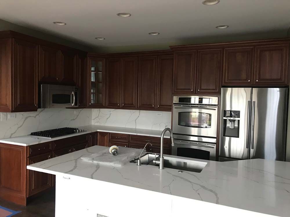Modern kitchen with dark wood cabinets, stainless appliances, and a white marble island counter