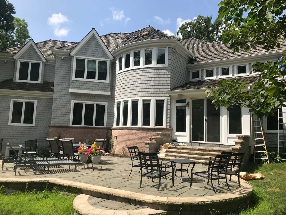 Large gray house with a curved patio, outdoor tables, chairs, and a ladder on the right side