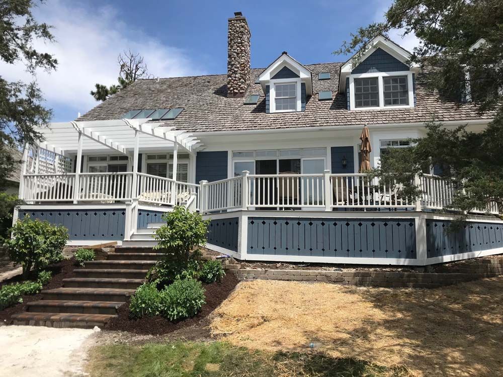 White house with front porch, steps, and dormer windows under a partly cloudy sky