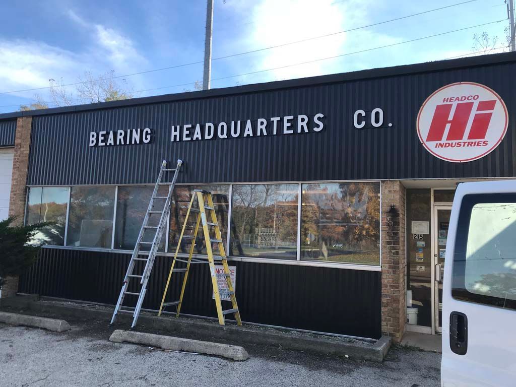 Exterior of Bearing Headquarters Co. storefront with ladders leaning against the building and a red logo sign