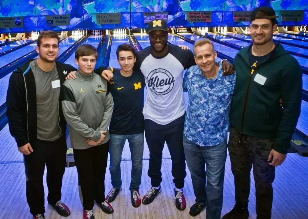 Six men pose together at an indoor event, standing in front of a blue-lit backdrop.
