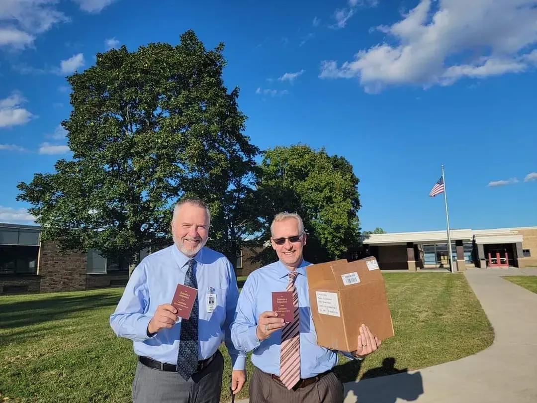 Two men holding cardboard signs and coffee cups outside a building on a sunny day