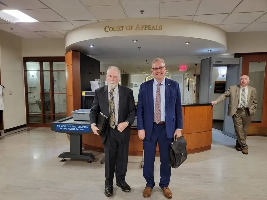 Two men in suits walking through a courthouse lobby with a reception desk and arched ceiling.