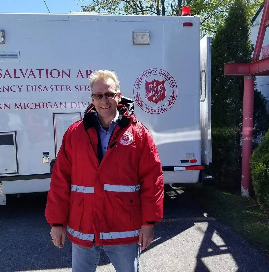 Man in red Salvation Army jacket standing outside a white Salvation Army vehicle
