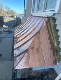 Freshly installed copper roof over a house window, with visible seams and wood siding.