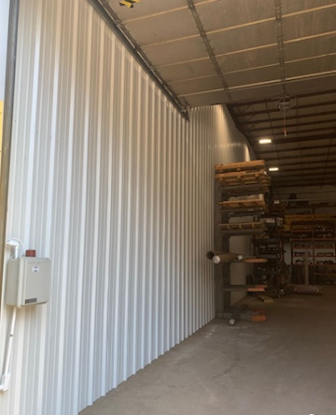 Interior of a warehouse with white corrugated wall, concrete floor, and stacked shelving in the background