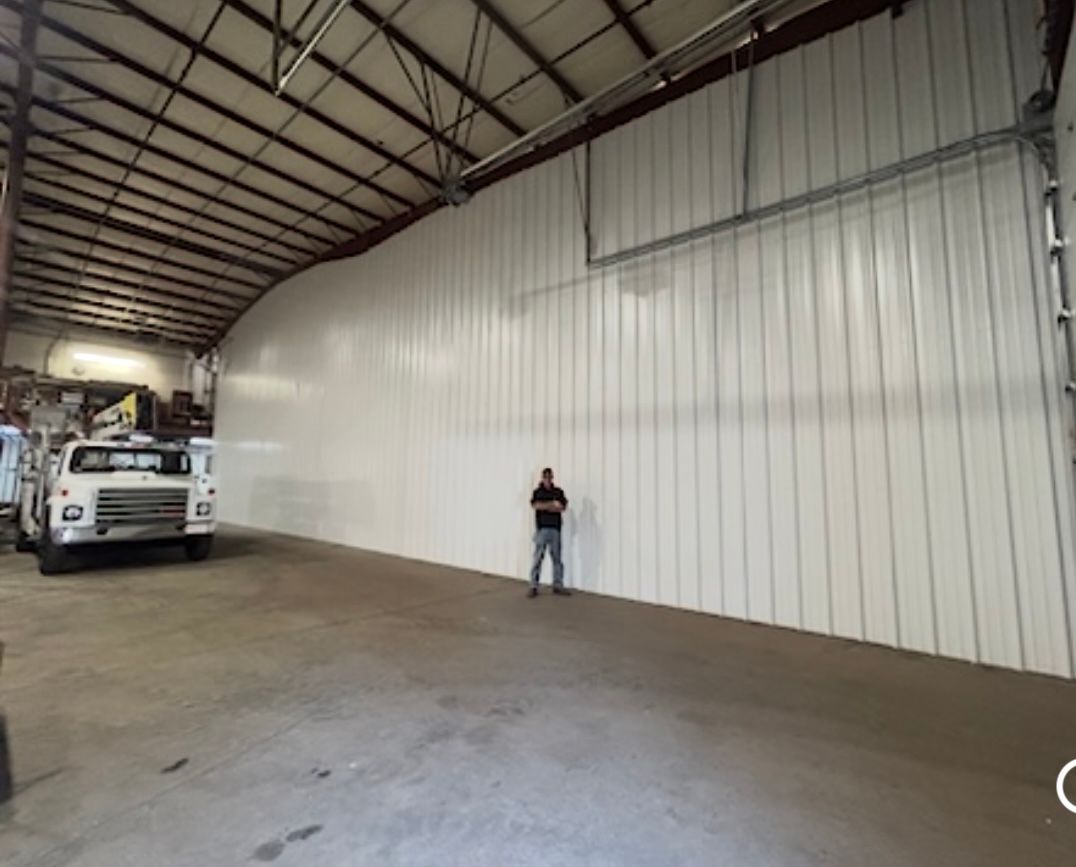 Large warehouse interior with a white wall, a parked truck, and a person standing near the wall