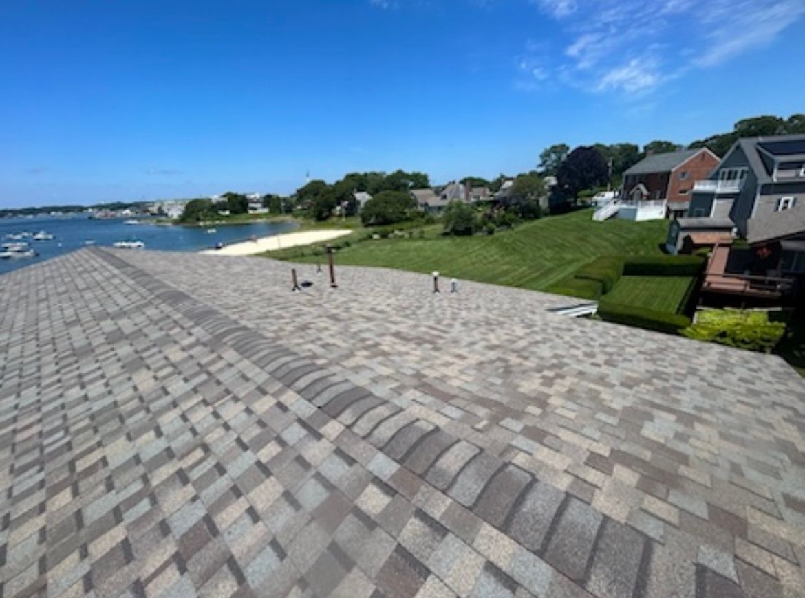Stone rooftop with a waterfront view, green lawn, and houses under a blue sky