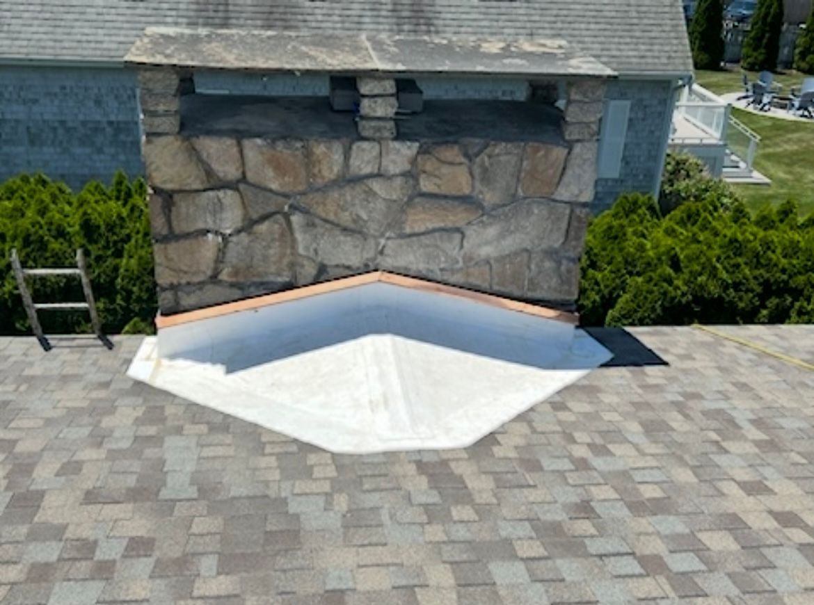 Stone retaining wall with a white concrete ramp in front of a house, surrounded by paved driveway.