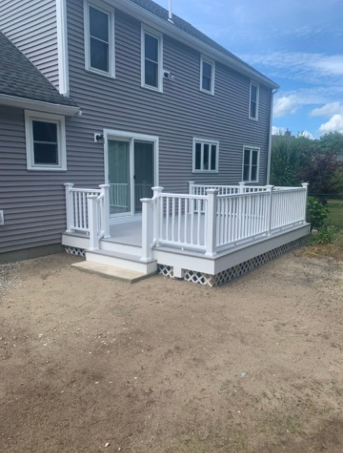 Backyard deck with white railing and steps beside a gray house on a gravel yard