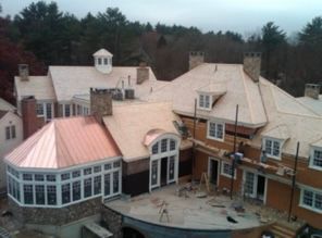 Aerial view of a large brick-and-cream mansion with a curved glass sunroom and rooftop cupolas surrounded by trees