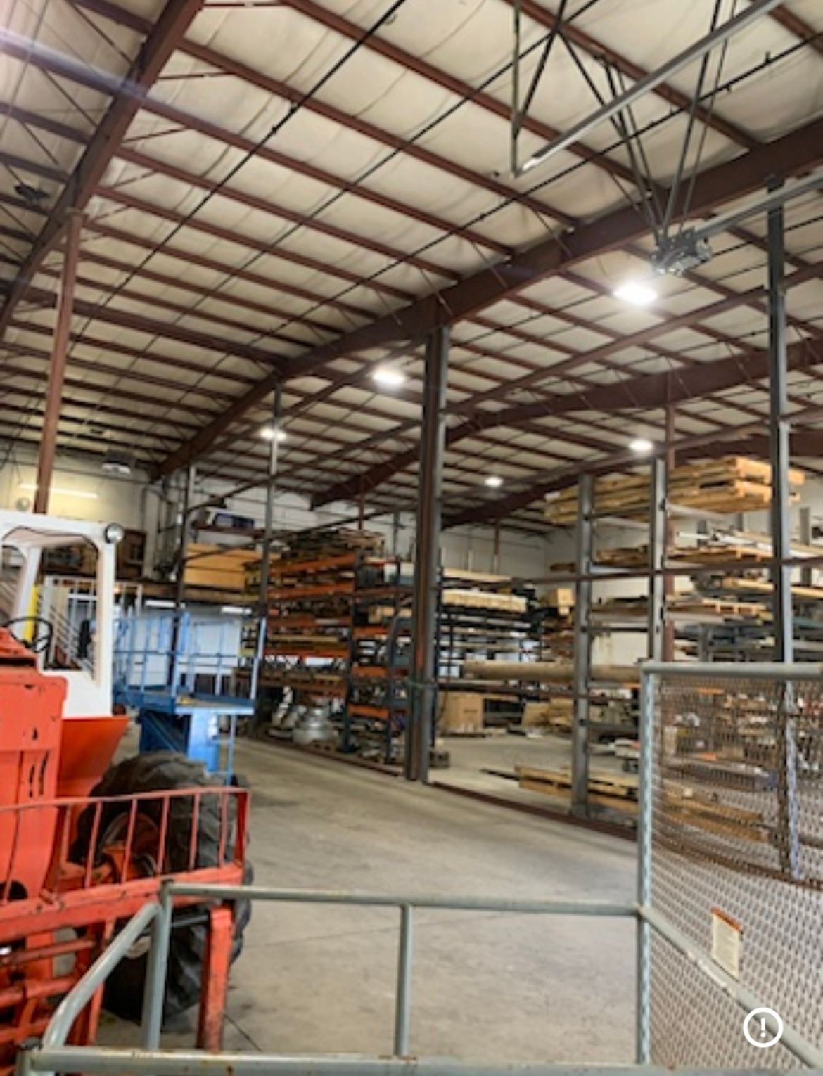 Large warehouse interior with steel shelving, stacked materials, and a red industrial machine in the foreground
