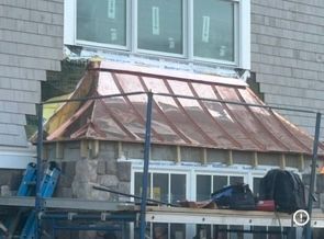 Copper roof under construction on a house, with scaffolding and blue tools beside a window.