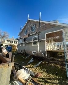 Two-story house with porch amid debris and yard clutter on a sunny day