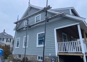 Gray two-story house with a front porch, white trim, and a ladder leaning against the roofline.