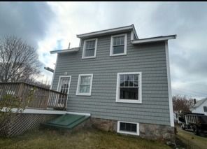 Gray two-story house with white trim, deck, and basement window under a cloudy sky
