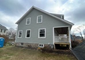 Gray two-story house with white trim, front porch, and cloudy sky in a suburban yard