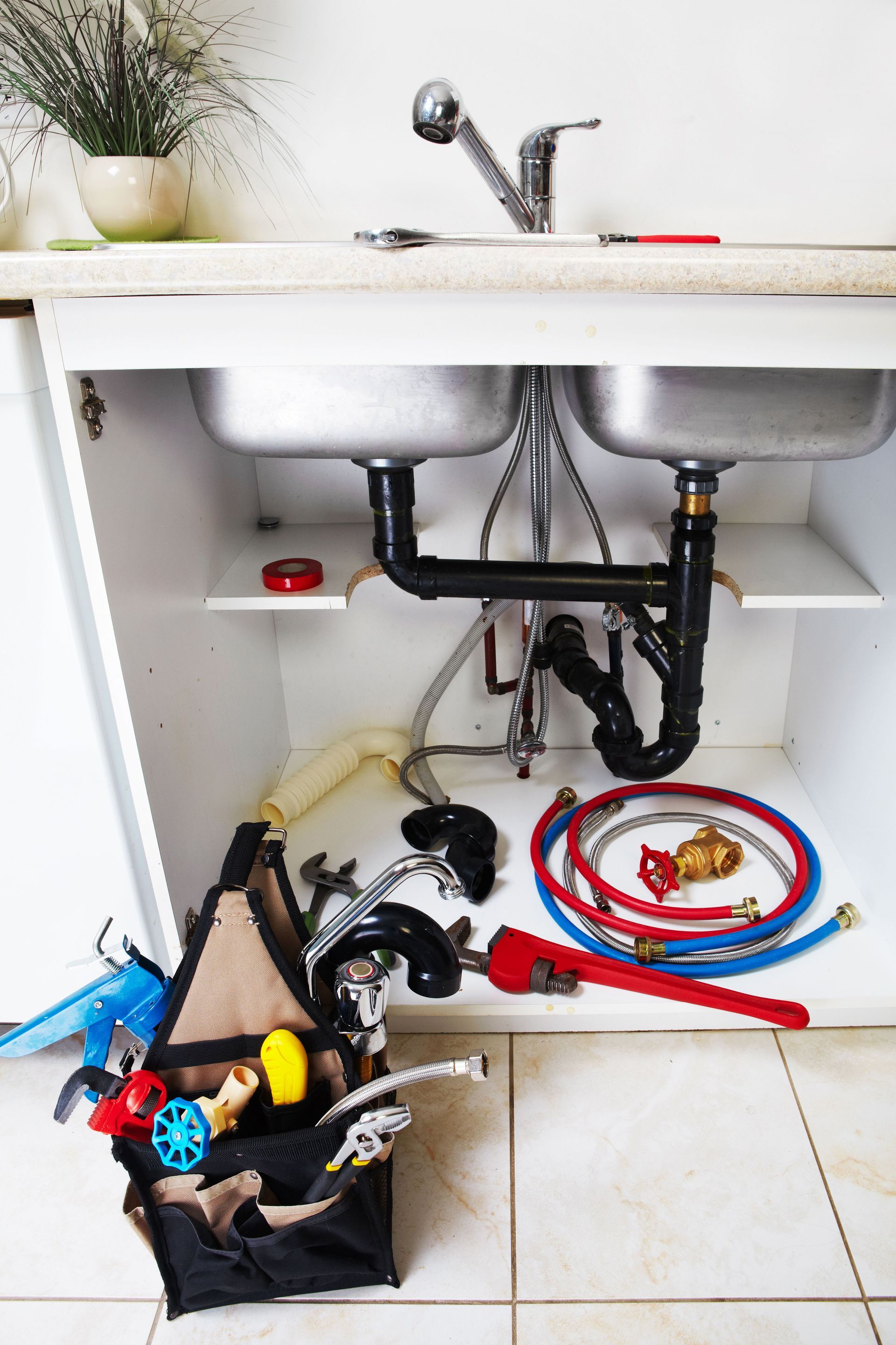 Under-sink plumbing area with tools and colored hoses scattered on the floor