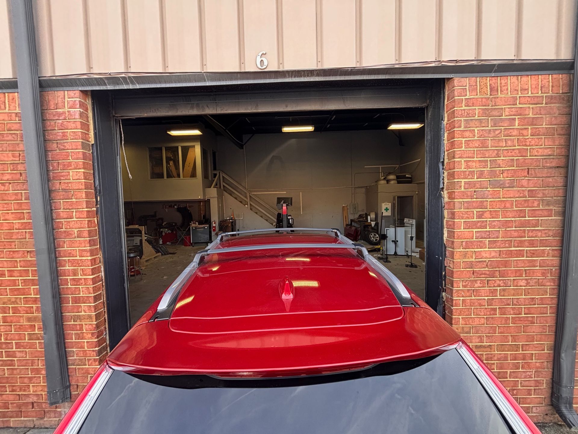 Red car entering a garage, framed by red brick and black supports. A person stands inside the garage.