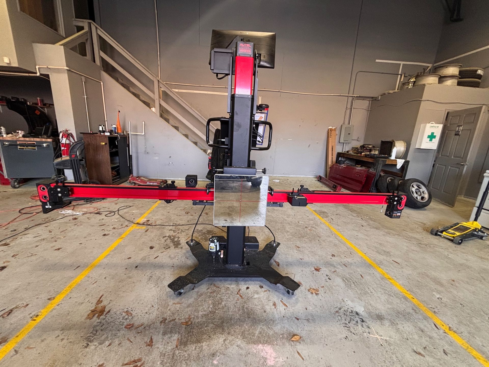 Wheel alignment machine in a garage. Red and black equipment on a concrete floor with yellow lines.
