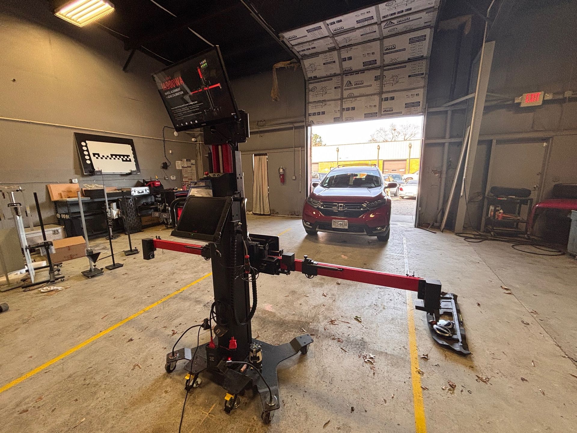 Wheel alignment machine in auto repair shop, car in background.