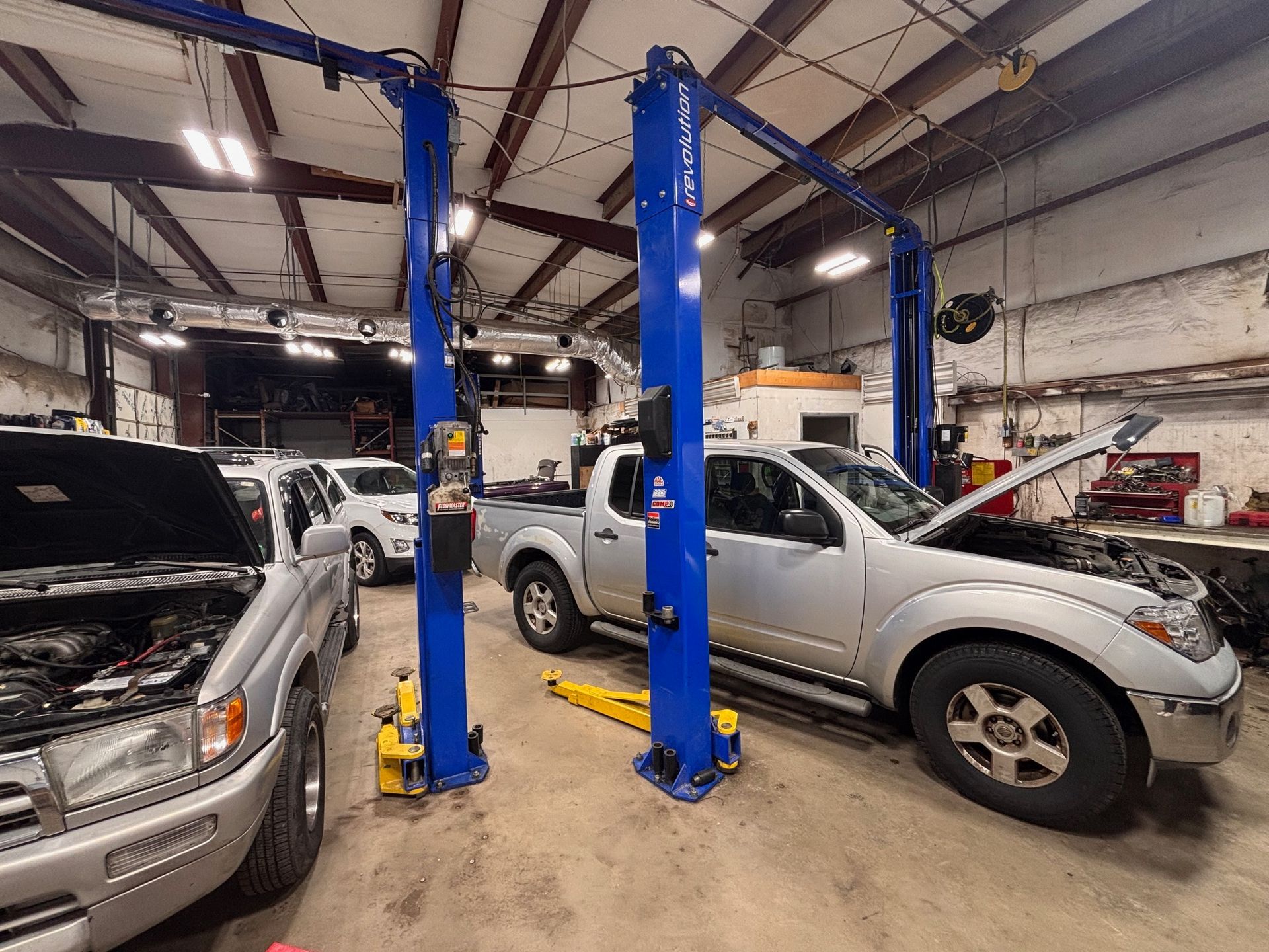 Cars in a repair shop, two on lifts. Two-post lifts are blue. One car hood is open.