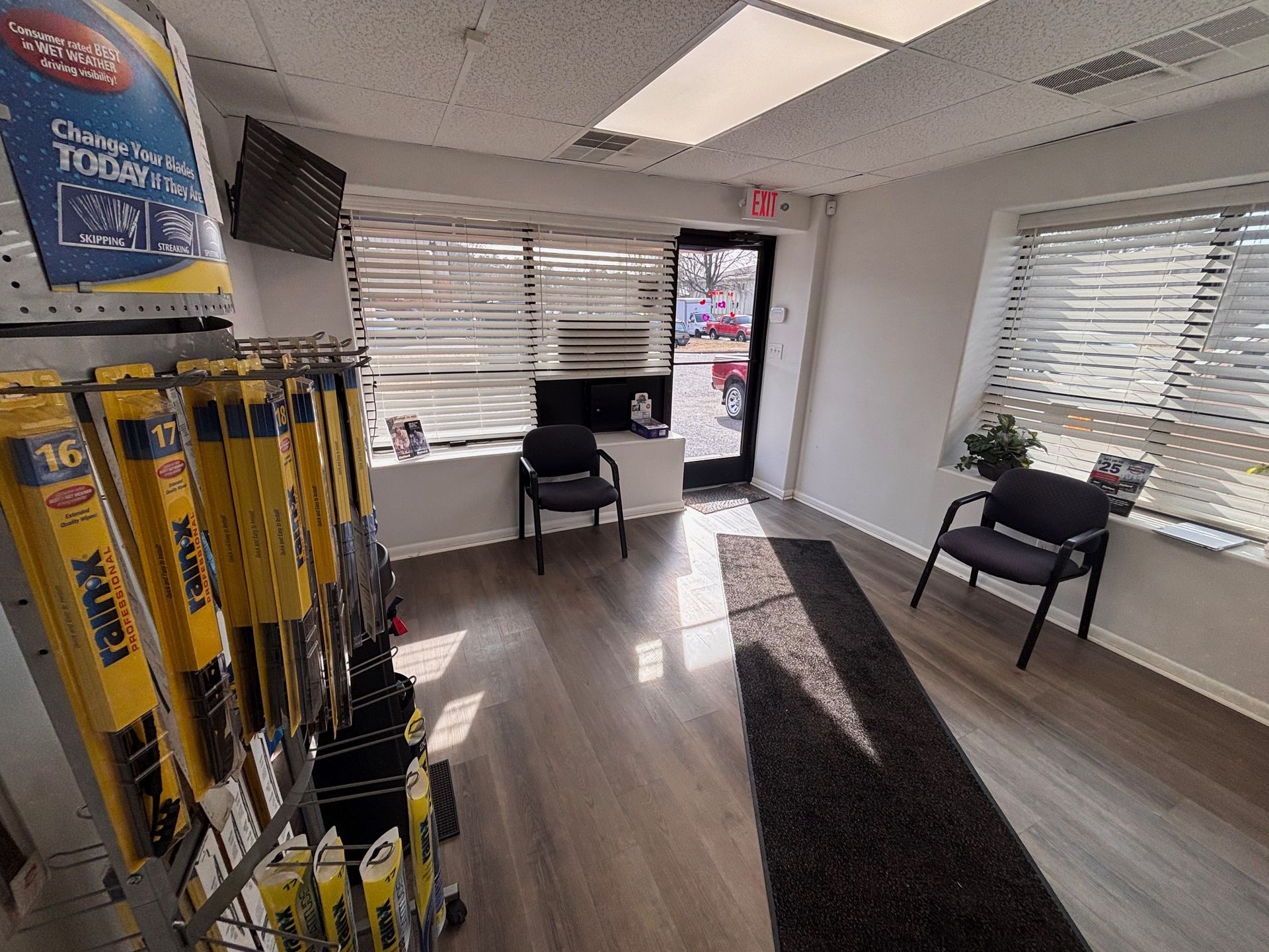 Waiting room with chairs, blinds, and a display of car parts. Bright interior.