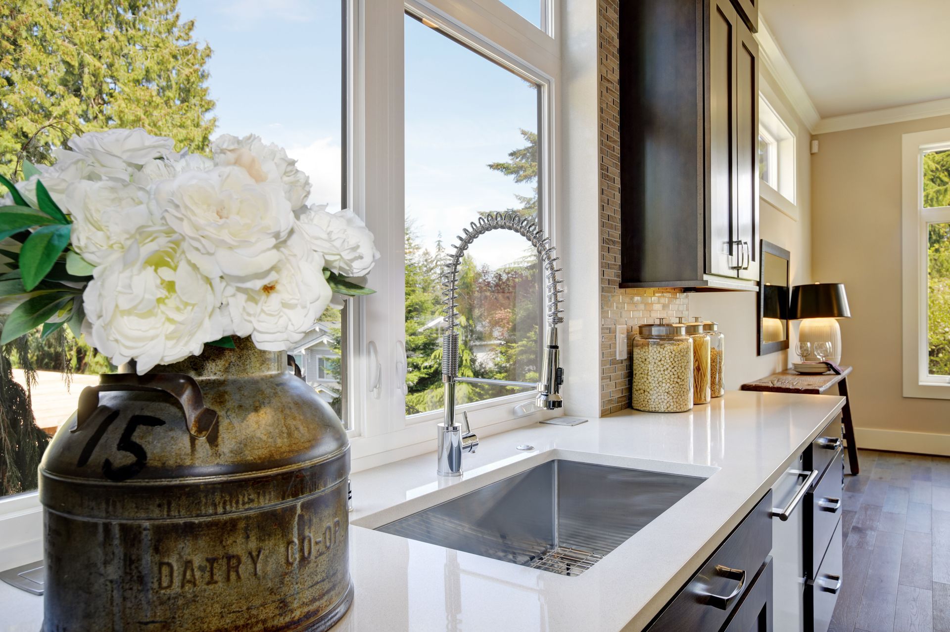 Bright kitchen with window, sink, white flowers, dark cabinets, and glass jars on the counter