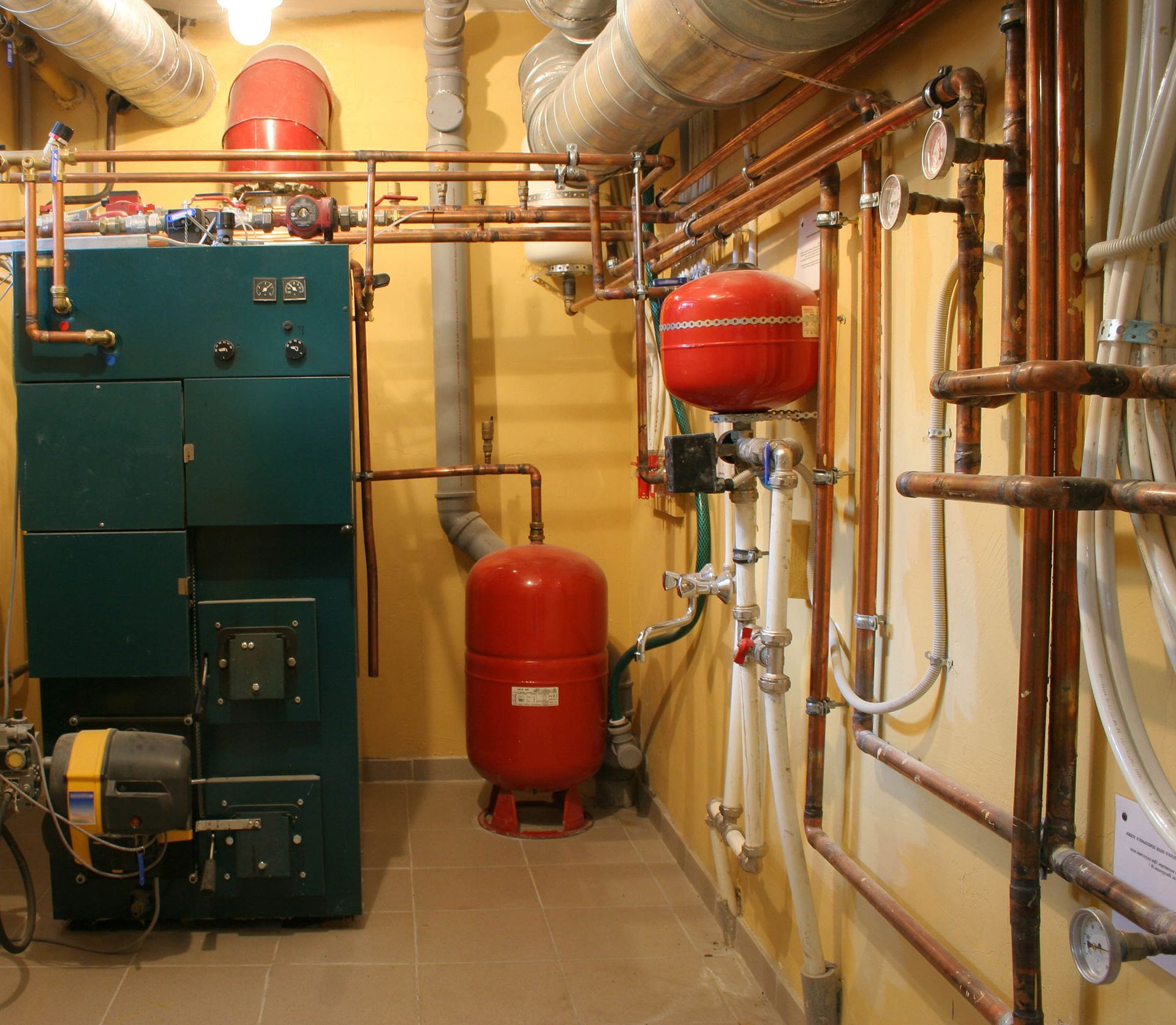 Boiler room with pipes, red tanks, and industrial heating equipment along yellow walls.