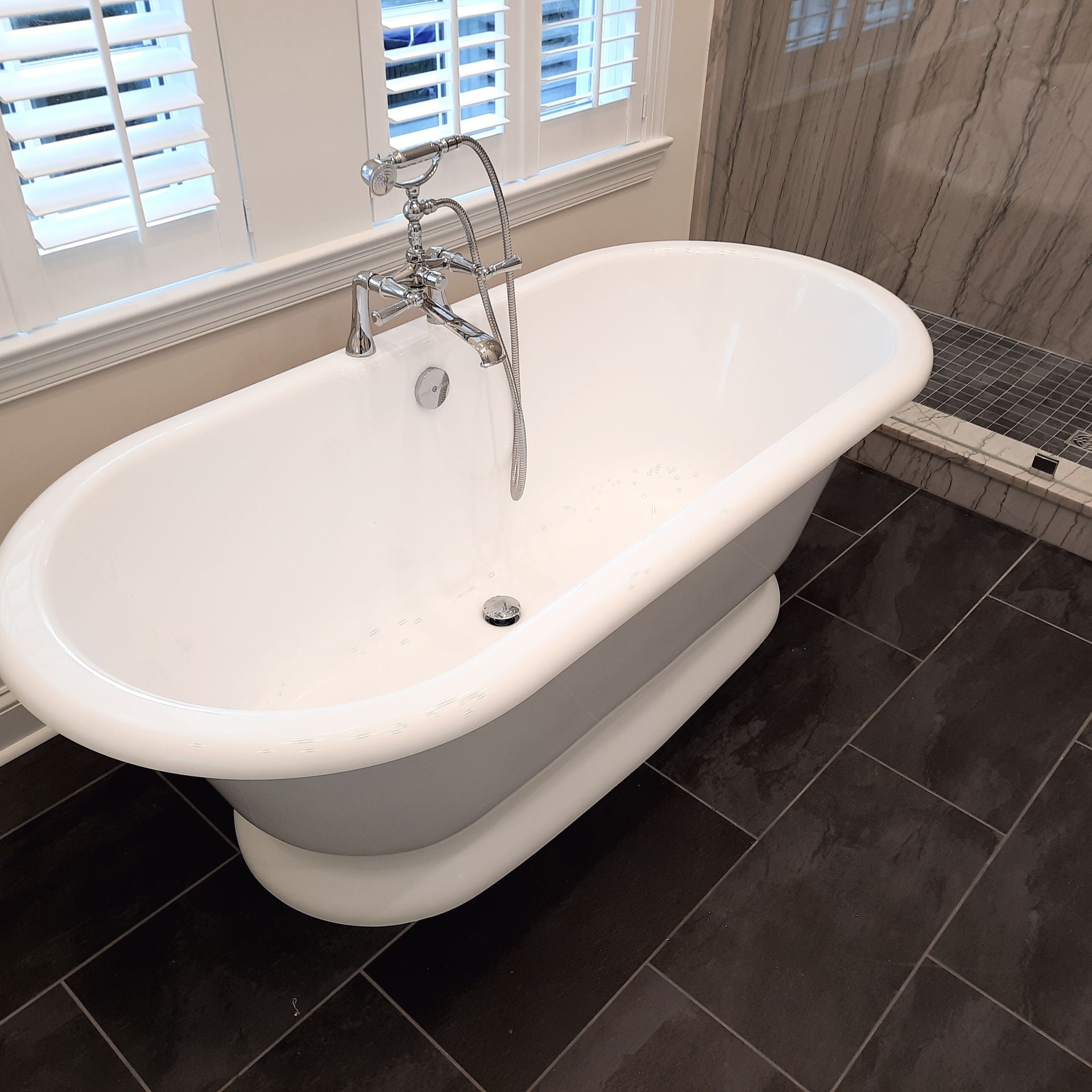 Freestanding white bathtub with chrome faucet in a tiled bathroom