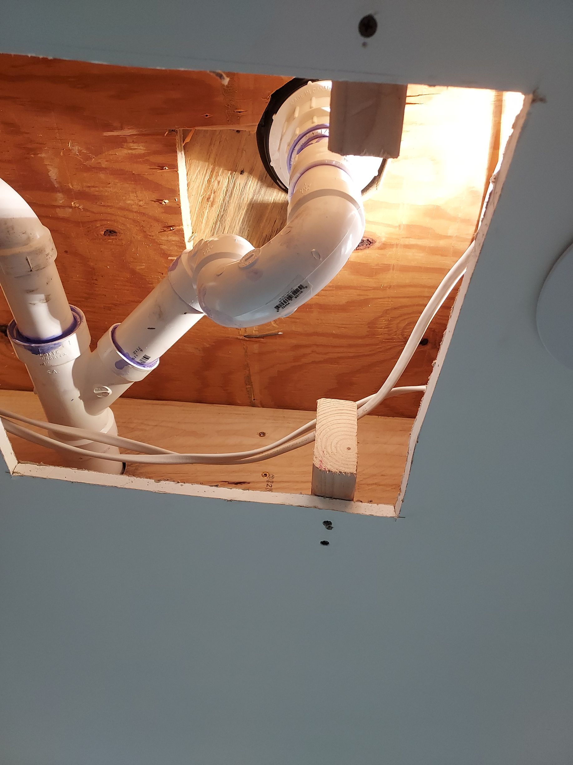 Open ceiling with exposed white PVC pipes and a flexible duct vent against wood framing and drywall.