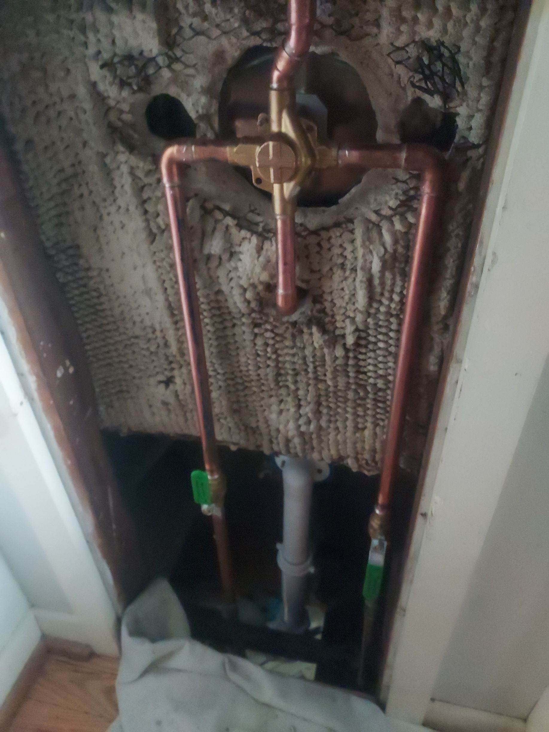 Exposed copper plumbing valves in a wall cavity with torn insulation and a cloth at the bottom.