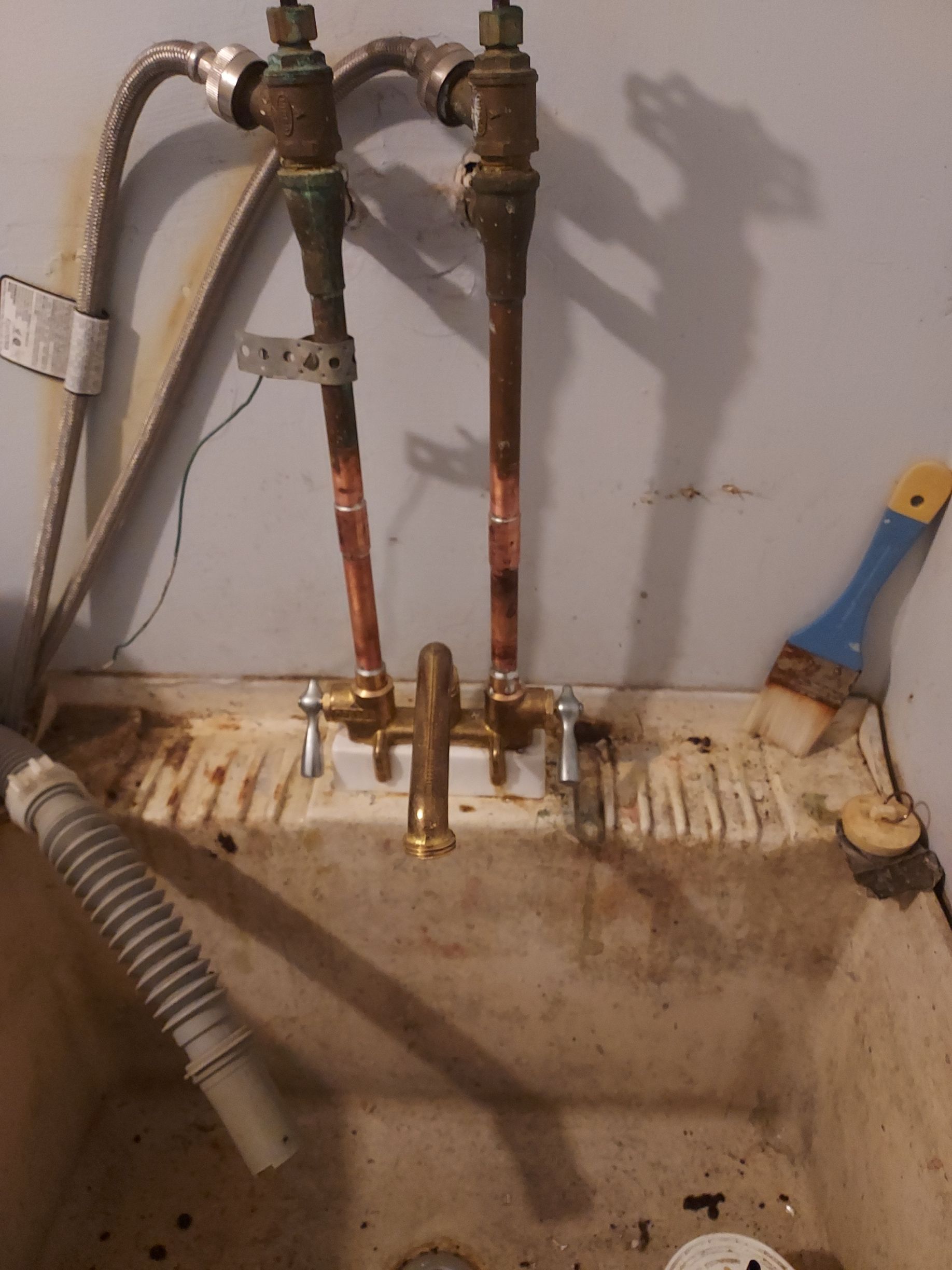 Utility sink with exposed copper pipes, faucet, and a corrugated drain hose against a wall.