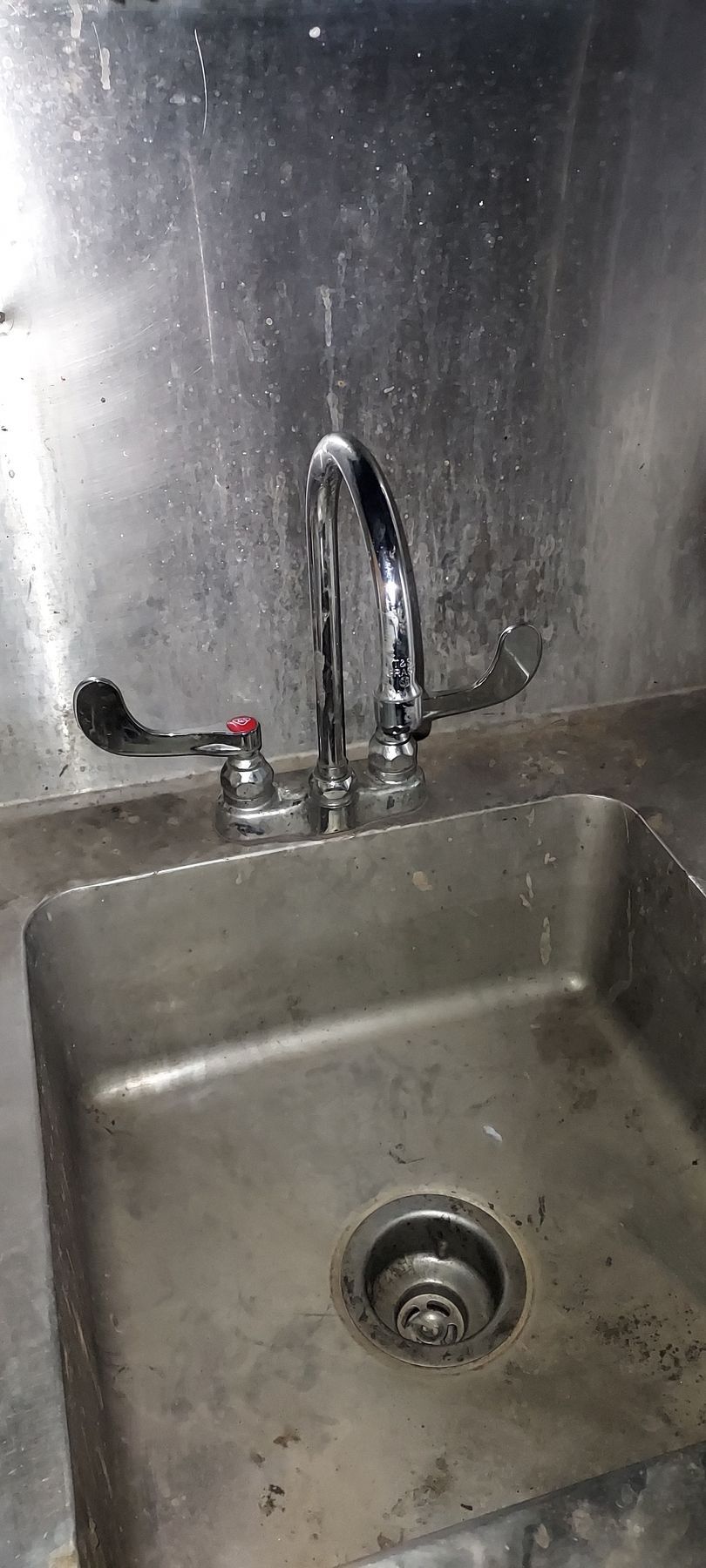 Stainless steel sink with faucet and drain in a metal kitchen or utility area.