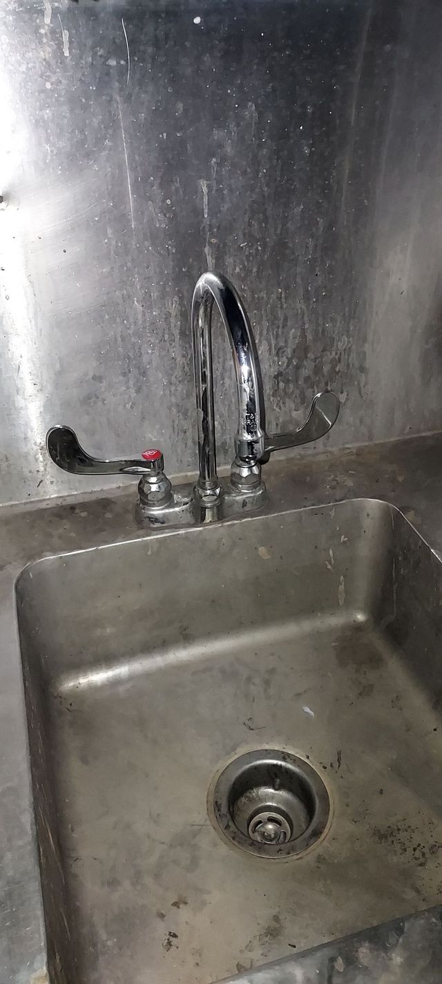 Stainless steel sink with faucet and drain in a metal kitchen or utility area.