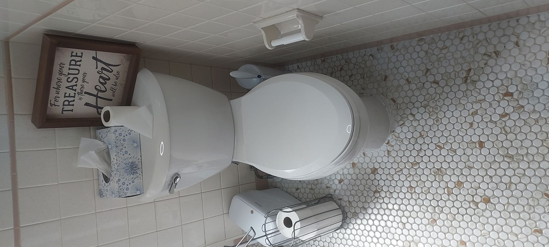 Small tiled bathroom with a toilet, sink, and framed sign above the tank.