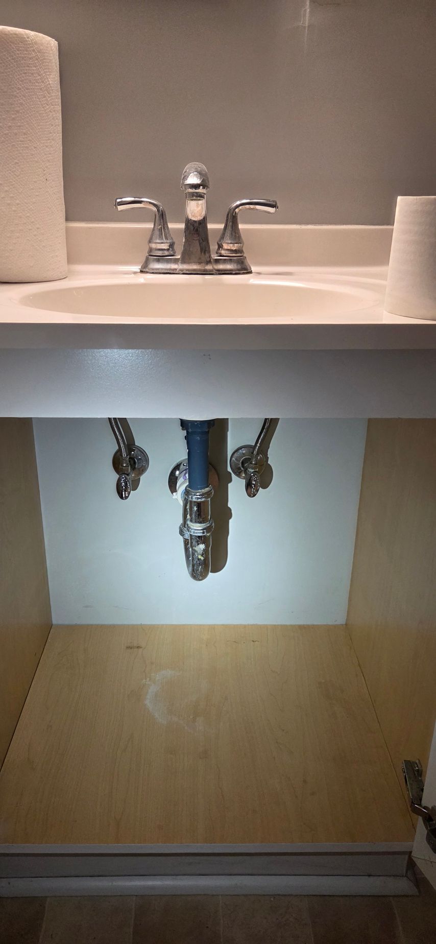 Bathroom sink with cabinet doors open, showing exposed plumbing and the inside of the vanity.