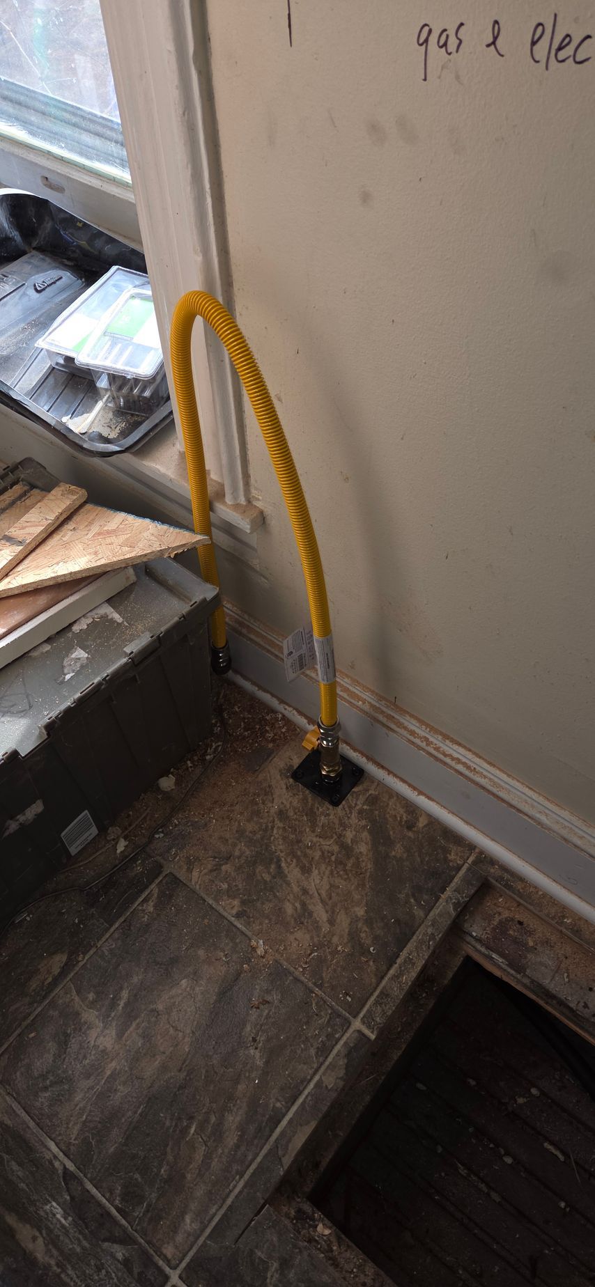 Yellow coiled hose on a dusty wooden floor beside a wall and stairwell.