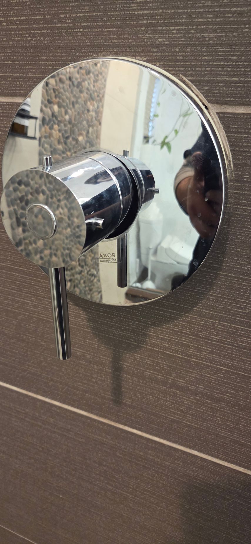 Close-up of a chrome shower control knob on a tiled bathroom wall.