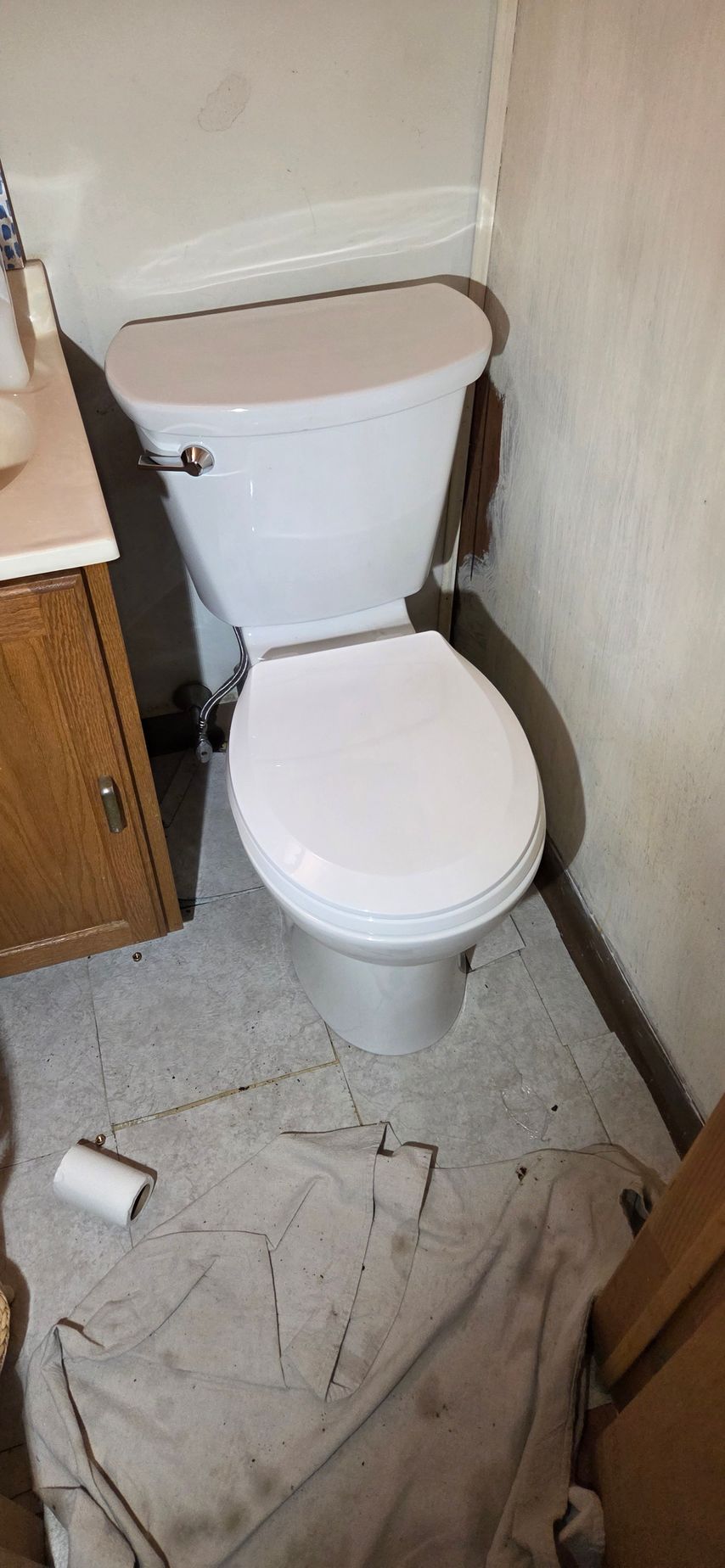 Small bathroom with a white toilet, cluttered floor, and narrow space beside a sink cabinet.