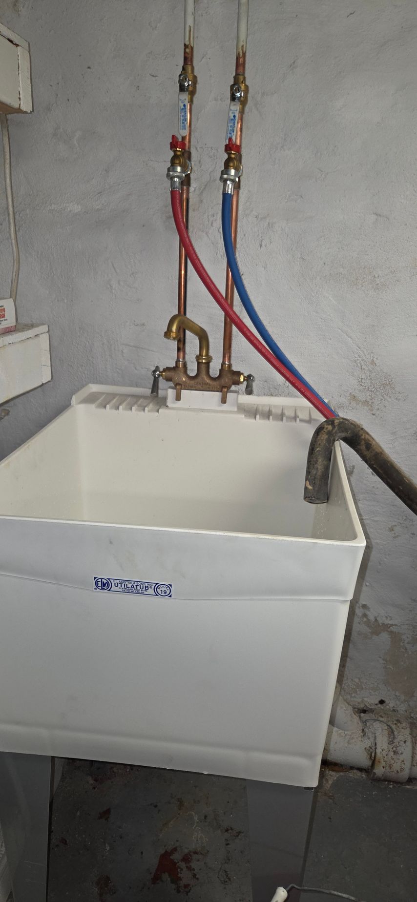 Small utility sink with exposed red and blue water pipes against a concrete wall.